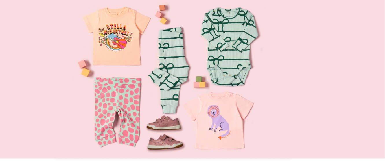 Pink background with a baby's outfit with a t-shirts, leggings, overalls, and shoes