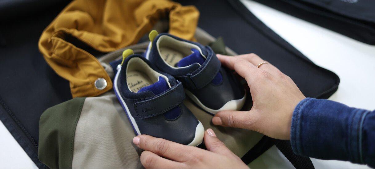 A parent holding a pair of dark blue babies shoes together on top of a waterproof jacket