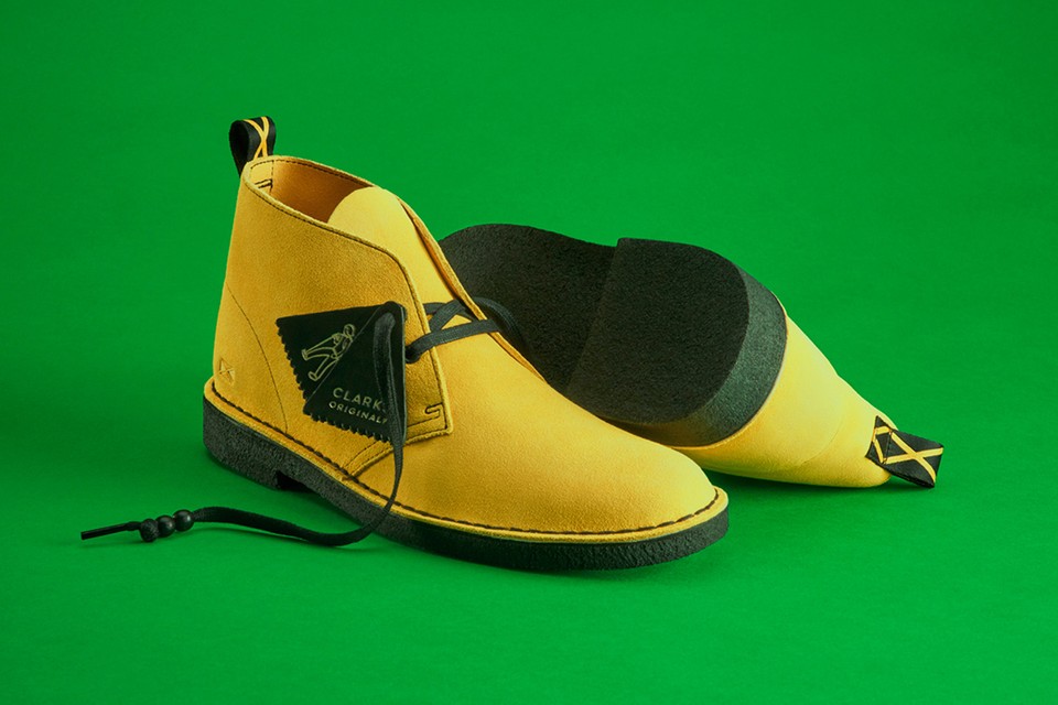 Close-up of a pair of yellow suede shoes on a green background. Dark green tag with the text 'Clarks Original' attached to the lase.