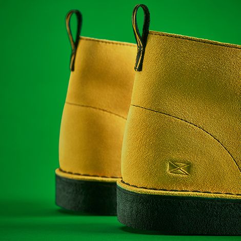 Close-up side view photo of yellow colored suede boots on a green background.